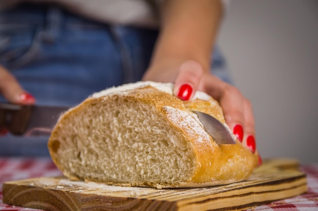 Belo pão sourdough sendo fatiado por faca pelas mãos da mulher e fundo desfocado