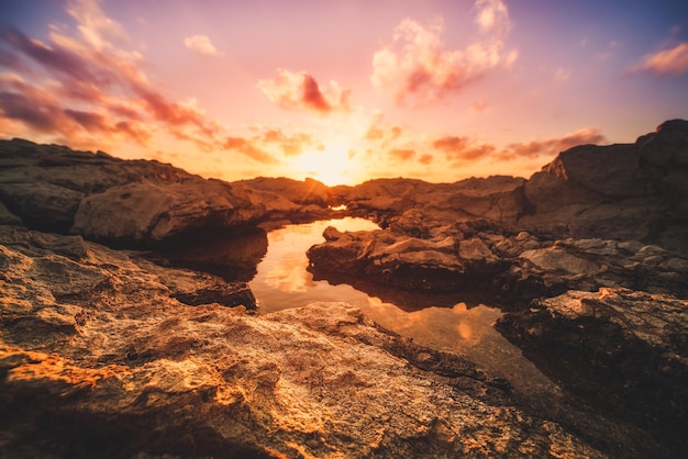 Belo pôr do sol colorido perto do mar em Chipre com nuvens dramáticas e pedregulhos Reflexões na água Fundo natural de viagens ao ar livre do mundo da beleza