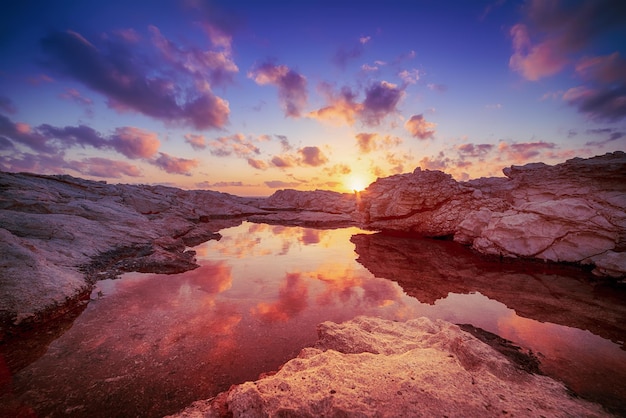 Belo pôr do sol colorido perto do mar em chipre com pedras e nuvens dramáticas. reflexos na água. fundo de viagens naturais ao ar livre do mundo da beleza