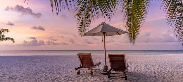 Belo pôr do sol da ilha tropical, guarda-chuva de cadeiras de espreguiçadeiras de casal sob folhas de palmeira. areia Branca