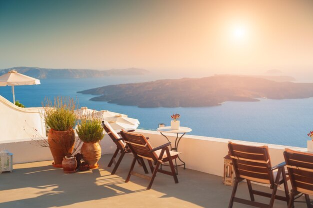 Belo pôr do sol na ilha de Santorini, Grécia. Cadeiras no terraço com vista mar. Destinos de viagens famosos