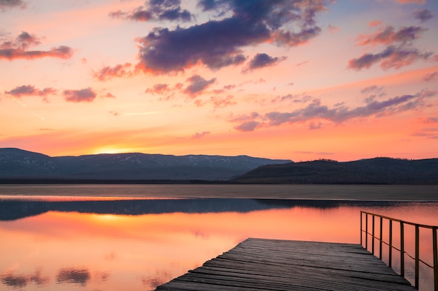 Foto belo pôr do sol na margem do lago no início da primavera. céu com nuvens refletidas na superfície da água calma. derretimento de gelo no lago. bashkortostan, rússia