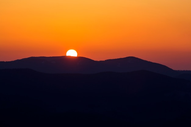 Belo pôr do sol nas montanhas. Vista panorâmica ampla do grande sol branco brilhante no céu laranja dramático sobre a paisagem de montanhas escuras no pôr do sol ou nascer do sol