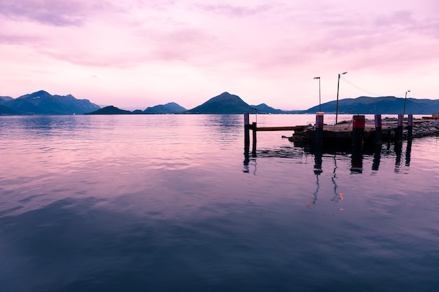 Belo pôr do sol no fiorde na Noruega. Montanhas com nuvens rosa e seus reflexos na água