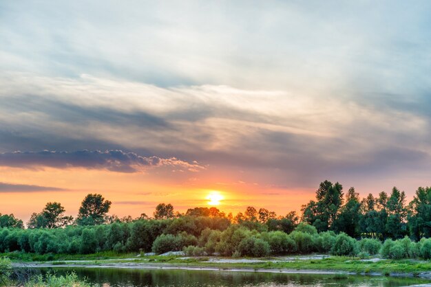 Belo pôr do sol sobre um grande rio com floresta verde na outra costa e reflexo na água