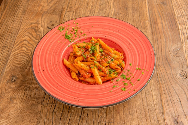 Foto belo prato de porcelana vermelha com receita de penne com tomate e salsa na mesa de madeira