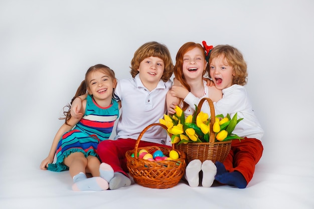 Belo retrato de crianças que se sentam junto com uma cesta de tulipas e uma cesta com ovos de Páscoa. Fundo branco. Momentos engraçados. Conceito de férias de primavera. Celebração da Páscoa em família.