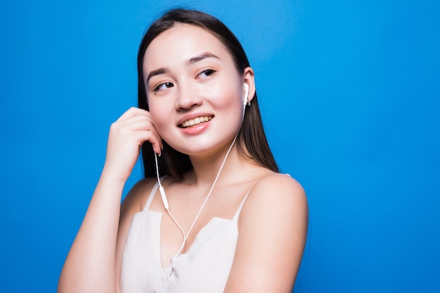 Belo retrato de jovem mulher asiática ouvindo música no telefone com fone de ouvido isolado na parede azul