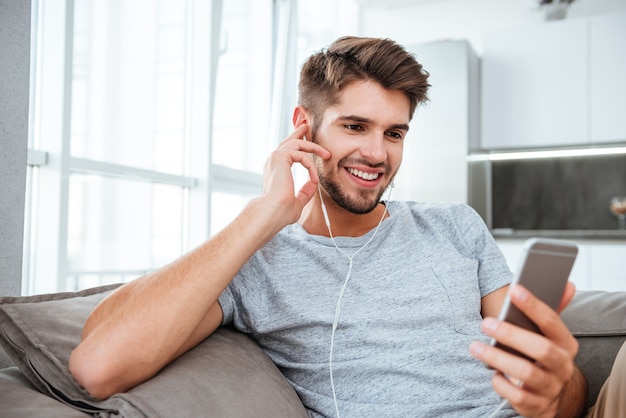 Belo retrato de jovem ouvindo música enquanto está no sofá e conversando.