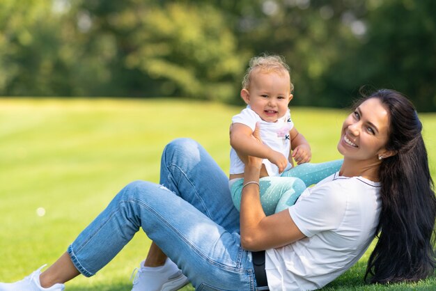 Belo retrato de uma alegre mãe e filho rindo para a câmera enquanto brincam juntos ao ar livre na grama verde em um parque ou jardim