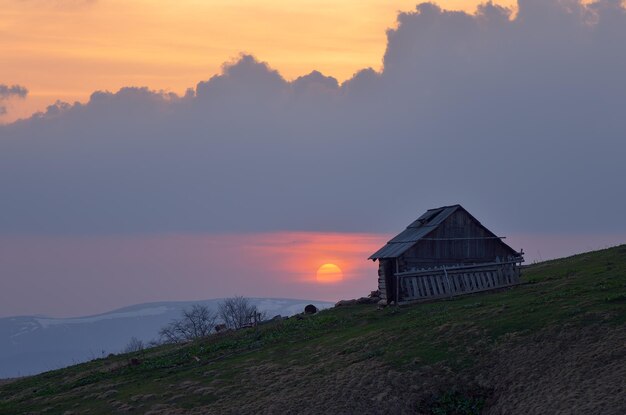 Belo sol ao pôr do sol. Antiga casa de madeira em uma colina de montanha. Pastores de residência. Cárpatos, Ucrânia, Europa