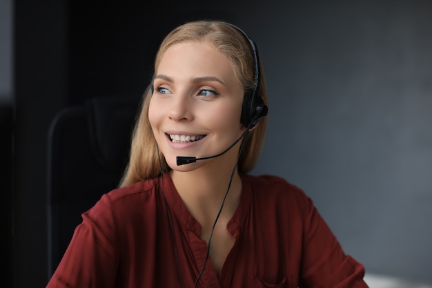 Belo sorridente call center trabalhador em fones de ouvido está trabalhando isolado sobre um fundo cinza.