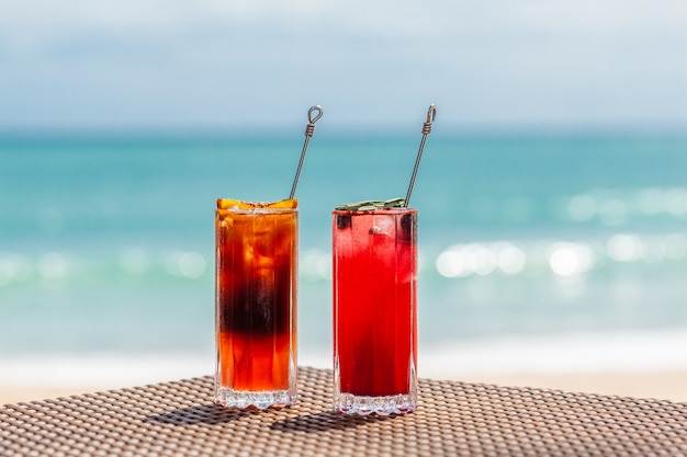 Belos coquetéis de frutas refrescantes na mesa na praia do mar azul no fundo