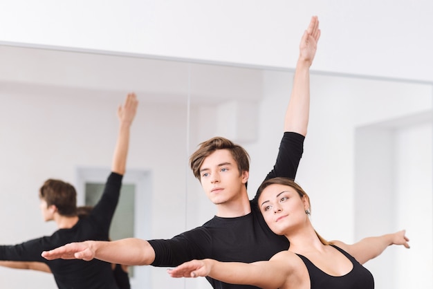 Belos movimentos. Dançarinos profissionais talentosos e persistentes em pé perto de cada um com as mãos para cima enquanto praticam a dança do balé