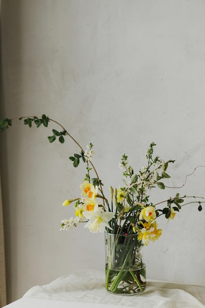 Belos narcisos, flores de cereja e composição de vegetação em vaso de vidro, bouquet de flores de primavera elegante em mesa rústica em sala rural, decoração moderna e simples de Páscoa