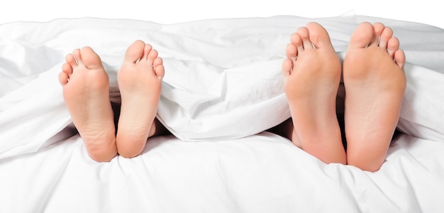 Belos pés de um jovem casal deitado na cama perto.