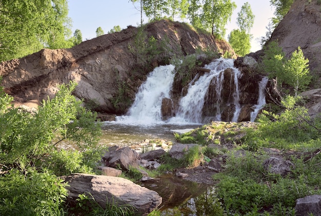 Belovsky Wasserfall im Frühjahr Ein kleiner Wasserfall zwischen den Felsen, umgeben von Birken