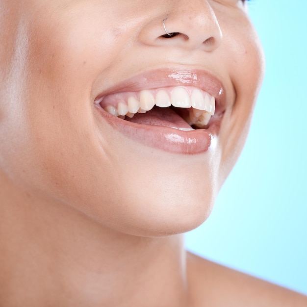 Bem-estar feliz e dentes de mulher odontológica com sorriso saudável higiene oral e zoom bucal Folheados de beleza e estética de clareamento dos dentes do jovem modelo de cosméticos em fundo de estúdio azul