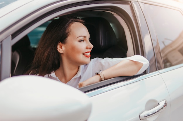 Bem sucedida elegante sorridente morena jovem bonita com lábios vermelhos, dirigindo o carro