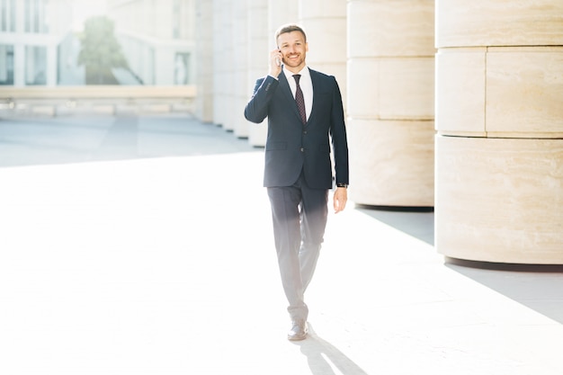 Bem sucedido empresário masculino em roupas formais, faz uma ligação telefônica para o parceiro via telefone celular