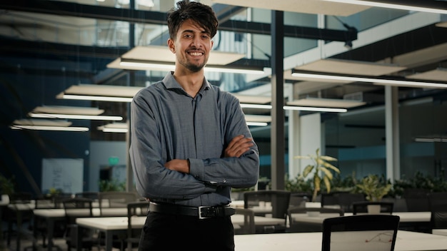 Bem-sucedido empresário sorridente indiano árabe posando no escritório com os braços cruzados com confiança