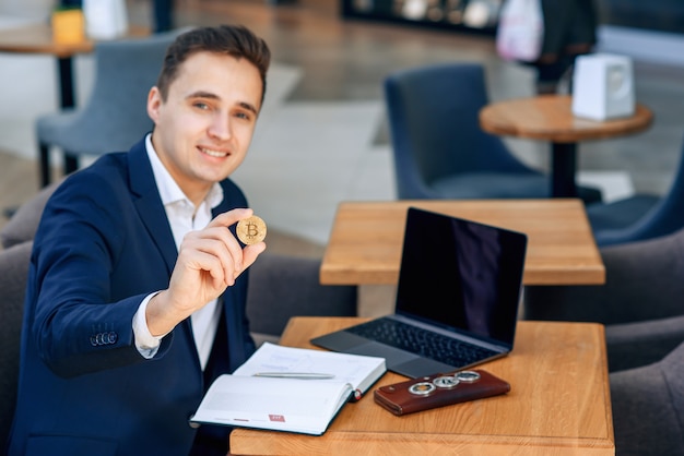 Bem sucedido empresário sorridente tem uma moeda de bitcoin de ouro na mão