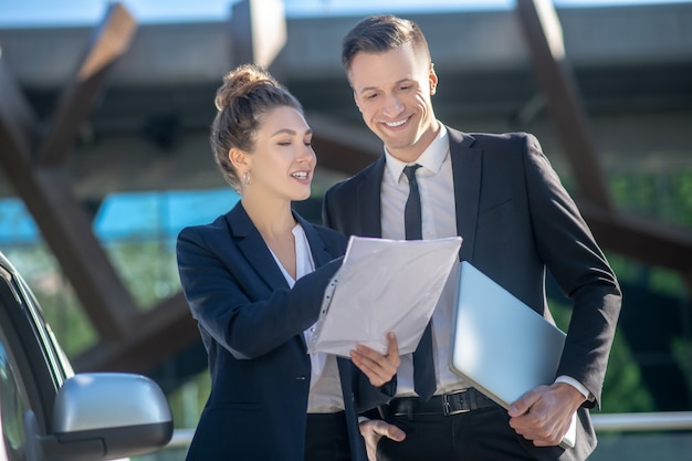 Bem sucedido homem confiante com laptop e mulher com documento.