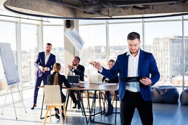 Bem-sucedido mentor masculino bonito, diretor, empresário de terno no escritório. Conceito de dia de trabalho. Reunião de equipe com o chefe em primeiro plano