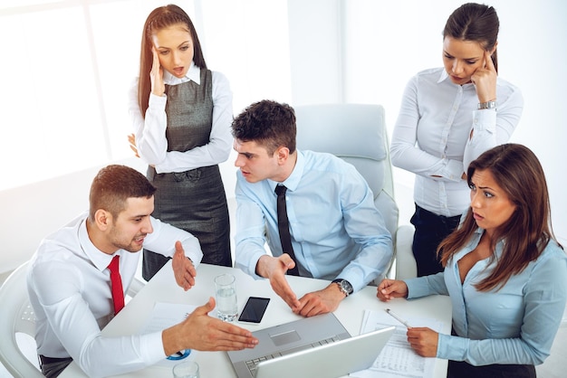 Bem sucedidos jovens colegas sorridentes trabalhando no laptop no escritório.