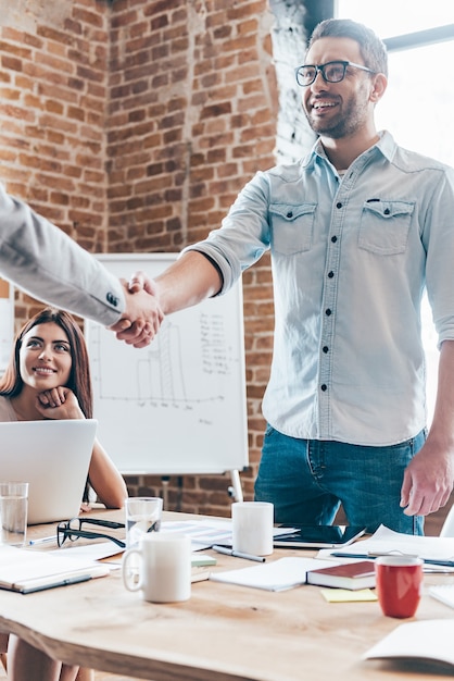 Bem-vindo a bordo! Dois empresários apertando as mãos em pé perto da mesa do escritório