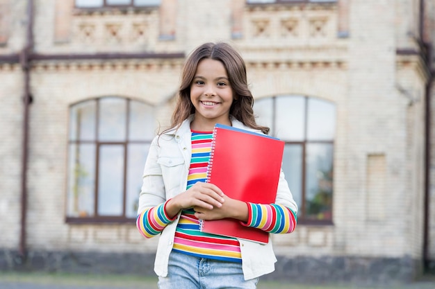 Bem-vindo à escola Bonita criança da escola primária sorrindo com livro na mão Garotinha feliz tendo aulas na escola primária De volta à melhor escola