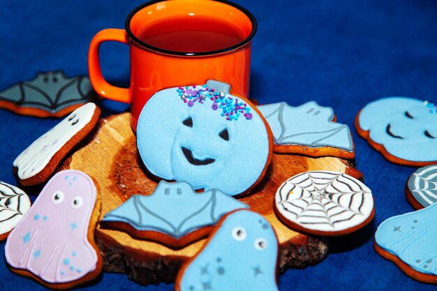 Bemalte Lebkuchen-Halloween-Plätzchen und eine orangefarbene Tasse auf blauem Hintergrund