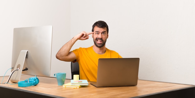 Bemannen Sie das Arbeiten mit laptot in einem Büro, das die Geste des Wahnsinns macht Finger auf den Kopf machend