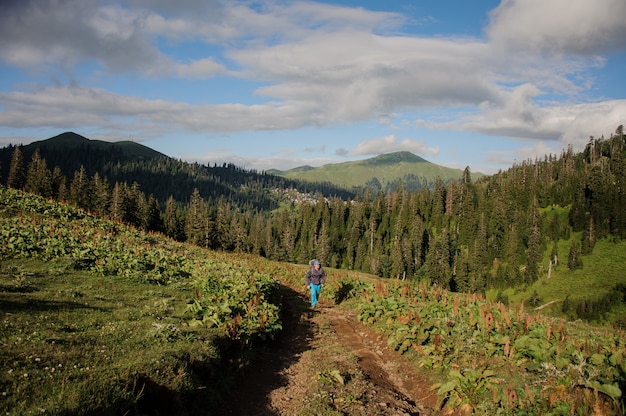 Bemannen Sie das Gehen auf den Schotterweg mit dem Wandern des Rucksacks und der Stöcke im Hintergrund des Baums bedeckte Hügel