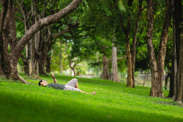 Bemannen Sie das Legen auf das Feld im Park und das Schauen und seinen Smartphone überprüfen