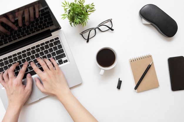 Bemannen Sie das Schreiben auf Laptop-Computer über weißer Schreibtischtabelle mit Tasse Kaffee und Büroartikel.