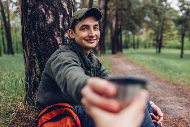 Bemannen Sie den Touristen, der seinem Waldkampieren des Freunds im Frühjahr Tasse heißen Tee gibt und reisen