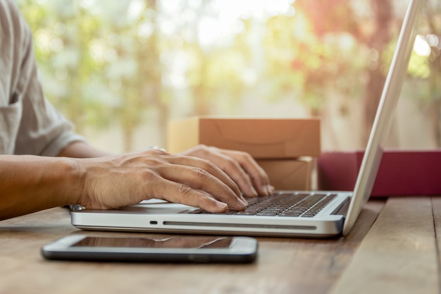 Bemannen Sie die Hände, die auf Laptoptastatur mit Paketpaketlieferung auf Tabelle schreiben.