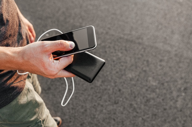 Bemannen Sie die Hände, die schwarzen Smartphone halten, der Batterie von der Bank der externen Energie auflädt