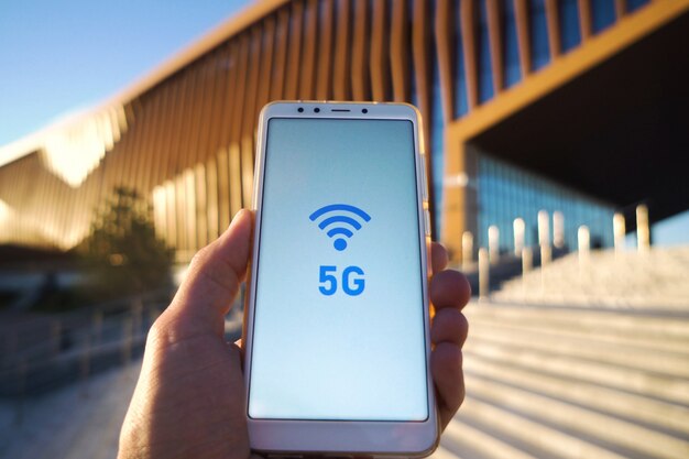 Bemannen Sie die Hand, die ein Smartphone- und 5g-Signalsymbol auf Schirm mit Sendeantenne hält. Mobiles Hochgeschwindigkeitsnetzverbindungstechnologiekonzept