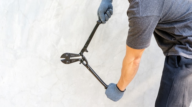 Bemannen Sie einen Handschuh tragen und das Halten der Ausschnittzangen auf grauem Hintergrund.