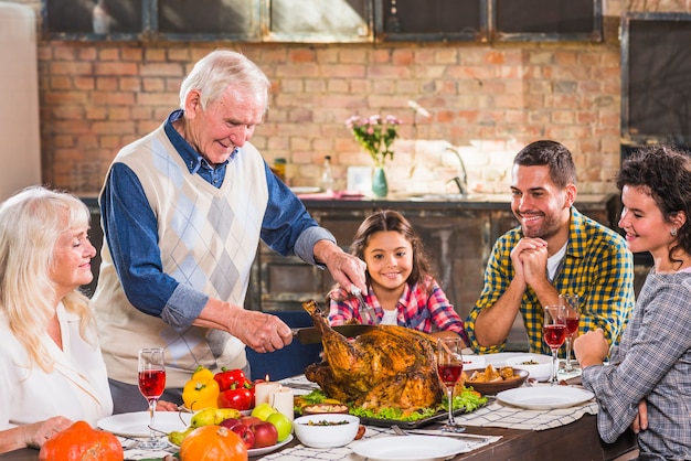 Bemannen Sie geschnittenes gebackenes Huhn bei Tisch mit Familie