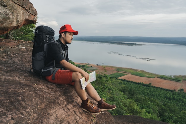 Bemannen Sie Reisenden mit dem Rucksack, der auf Rand der Klippe, auf eine Oberseite des Felsenberges sitzt