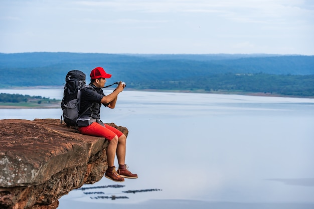 Bemannen Sie Reisenden mit Rucksack unter Verwendung der Kamera, die ein Foto auf Rand der Klippe, auf eine Oberseite des Felsenberges macht