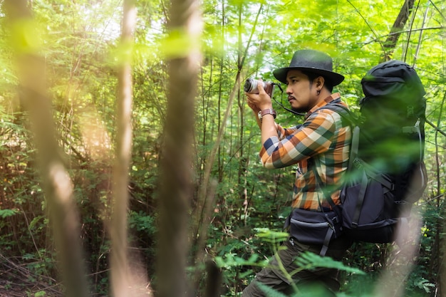 Bemannen Sie Reisenden mit Rucksack unter Verwendung der Kamera, um ein Foto im Wald zu machen