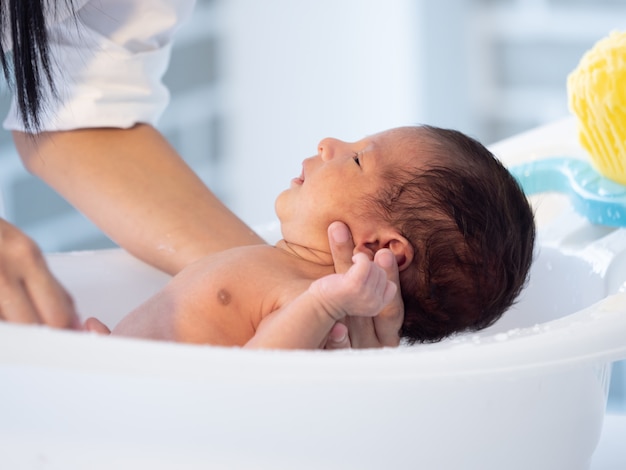 Bemuttern Sie das asiatische Jungenbaby des Bades, das auf der Badewanne neugeboren ist