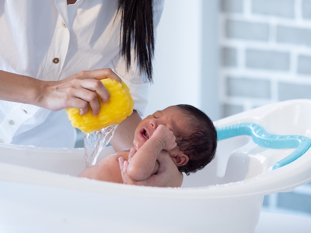 Bemuttern Sie das asiatische Jungenbaby des Bades, das auf der Badewanne neugeboren ist