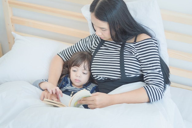 Bemuttern Sie das Lesen eines Bettzeit-Geschichtenbuches zu ihrer Tochter im Schlafzimmer.