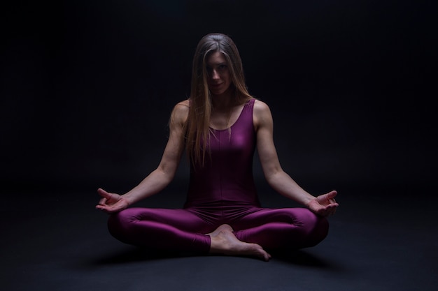 Übende Yogaposition der jungen Frau in der Lotosblume, lokalisiert auf einem dunklen Hintergrund