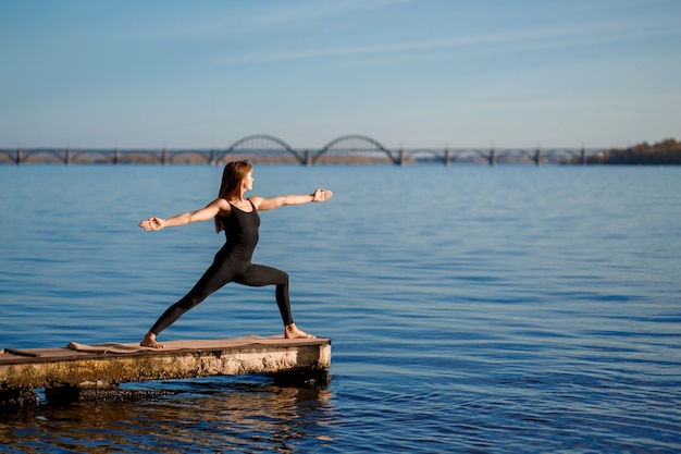 Übende Yogaübung der jungen Frau am ruhigen hölzernen Pier